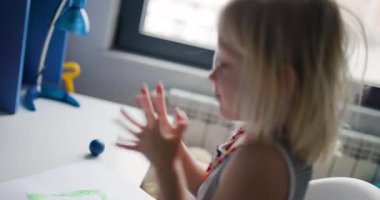 Şirin küçük bir kız masasında renkli modelleme kiriyle çizim yapıp oynamaktan zevk alıyor. Bu iç açıcı sahne çocukluğun neşe ve hayal gücünü yakalar..