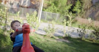 Genç bir çocuk oyun parkında kırmızı bir sallanan atın üzerinde oynamaktan hoşlanıyor. Bir ileri bir geri sallanırken gülümsüyor, dışarıda geçirdiği zamanın tadını çıkarıyor..