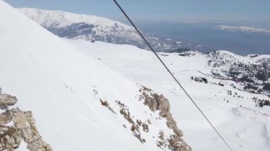 Kayakçılar, nefes kesen manzara ve açık mavi gökyüzü ile çevrili bir dağ sırasının nefes kesici karlı yamaçlarında, kış sporlarının neşesini gözler önüne sererek gezinirler..