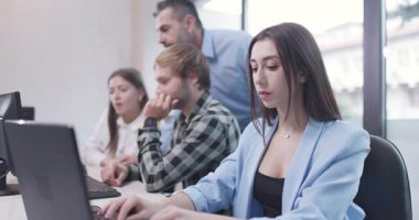 Ofiste dizüstü bilgisayarla çalışan bir kadın. İş arkadaşları arka planda birlikte çalışıyor. Sığ alan derinliği. 