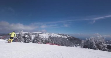 Bir kayakçı, görkemli dağ manzaralarıyla çevrili aydınlık bir kış gününde karlı yamaçlarda gezinir. Taze toz zemini kaplar, deneyimi güçlendirir..