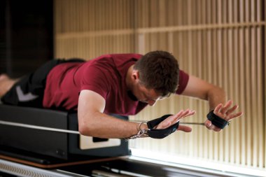 Pratikçi, çağdaş bir fitness stüdyosunda çekirdek dayanıklılık ve istikrarın vurgulandığı bir reformist pilates makinesi kullanarak kontrollü bir egzersiz gerçekleştirir..