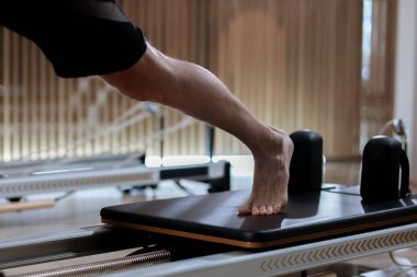 Katılımcılar, reformcu pilates makineleri üzerinde alıştırmalar yaparak, iyi aydınlatılmış bir stüdyo ortamında çekirdek istikrar ve esnekliği vurguluyor, fitness ve sağlığa olan bağlılığı sergiliyorlar..