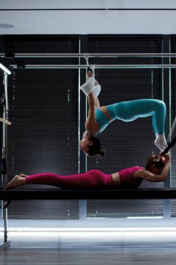 İki birey, yenilikçi pilates makineleri üzerinde senkronize bir çalışma gerçekleştiriyor. Parlak ve çağdaş bir stüdyo ortamında güç ve esneklik sergiliyorlar..