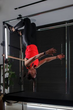 Modern bir fitness stüdyosunda, bireyin biri gelişmiş bir pilates çalışmasını bir yenilikçi makine üzerinde gerçekleştirir, odaklanmış bir eğitim oturumu sırasında hassas hareketlerle güç ve esneklik gösterir..