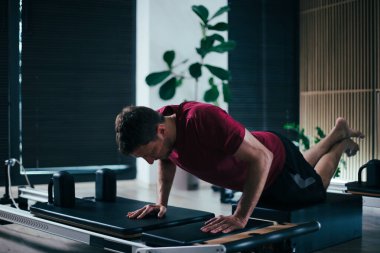 Pratisyen, gösterişli bir stüdyoda, doğal ışıklandırmalı, yenilikçi bir pilates makinesi üzerinde zorlu bir çalışma gerçekleştiriyor. Atmosfer konsantrasyon ve konsantrasyon artışını teşvik eder..