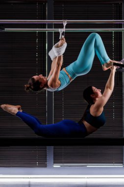 İki kadın karmaşık bir akrobatik rutine giriyorlar. İyi ışıklandırılmış kapalı bir tesiste spor salonunun barlarında sallanırken güç ve esneklik gösteriyorlar..