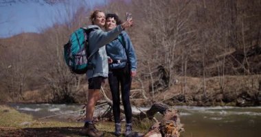 İki bayan arkadaş doğa yürüyüşü yaparken nehirde selfie çekiyorlar. Birlikte eğleniyorlar, fotoğraf çekiyorlar ve gülüyorlar..