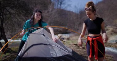 İki bayan arkadaş nehrin yanında çadır kuruyor. Birlikte çalışıyorlar ve dışarıda eğleniyorlar..