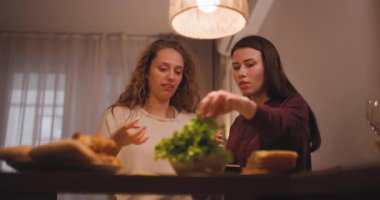 İki genç kadın yemek masasına sıcak ışıkla aydınlatılarak sıcak, dostane bir atmosfer yaratarak sandviç ve meyve suyu döker..