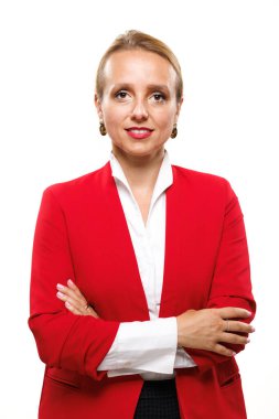 Bir iş kadını, kırmızı ceket ve beyaz bluz giyen, kolları çaprazlanmış bir şekilde güvenle ayakta duruyor. Parlak fon, stüdyo ortamında profesyonelliğinin ve liderlik vasıflarının altını çiziyor..