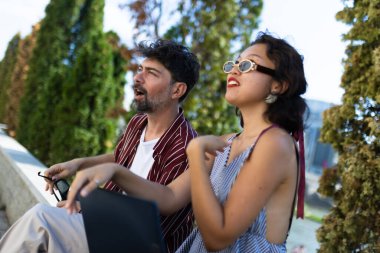 İki arkadaş, yemyeşil çimenliklerle çevrili açık havada canlı bir sohbete girişiyor. Rahat ve rahat görünüyorlar, güneşli bir günün tadını çıkarıyorlar..
