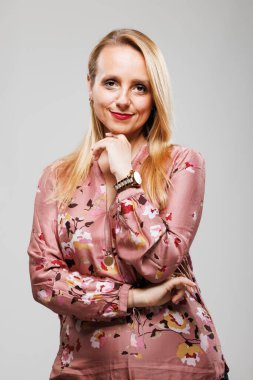 Kendine güvenen bir iş kadını kollarını kavuşturmuş, sıcak bir şekilde gülümsüyor. Çiçekli bir bluz giyer, profesyonelliğini göstererek sade, tarafsız bir stüdyo arkaplanı kullanır..