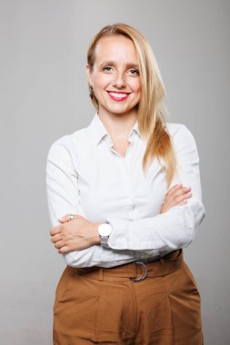 Kendine güvenen bir iş kadını kollarını kavuşturup profesyonellik gösteriyor. Açık renk bir gömlek ve şık bir pantolon giyiyor. Modern ve cana yakın bir iş tutumu sergiliyor..