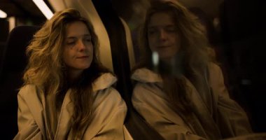 Genç bir kadın trenin penceresinin önünde oturuyor, derin düşüncelere dalmış, dışarıdaki dünya hareket ederken. İfadesi seyahati sırasında derin düşüncelere ve sakinliğe dair bir karışımı ortaya koyuyor..