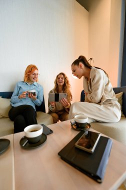 Üç iş kadını modern bir salonda oturup, bir fincan kahve eşliğinde fikir ve kahkaha paylaşıyorlar. Parlak alan, öğleden sonraki toplantı sırasında enerji dolu işbirliklerini arttırır..