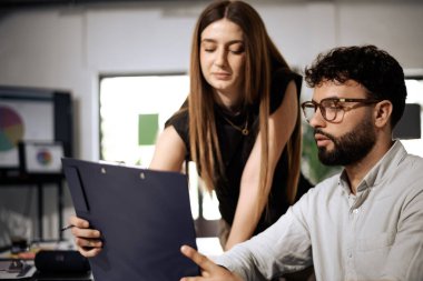 İki iş adamı, çalışma materyalleri ve çizelgeleri ile çevrili bir proje hakkında bir tartışmaya girişerek, modern ofis ortamındaki belgelere odaklanıyorlar..