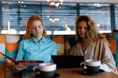 İki kadın şık bir kafede menüyü gözden geçirirken bir iş görüşmesinde bulundu. Odaklanmış ve profesyonel görünüyorlar, dostça bir toplantı sırasında kahvelerinin tadını çıkarıyorlar..