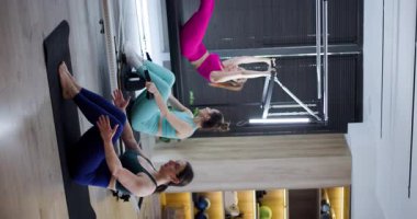 Üç kadın egzersiz malzemeleriyle dolu iyi aydınlatılmış bir stüdyoda pilates yapıyor. Çekirdeklerini güçlendirmeye ve çeşitli hareketlerle esnekliklerini artırmaya odaklanırlar..