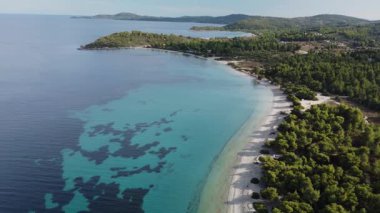 Yunanistan 'da berrak gökyüzünün altında turkuaz suyla buluşan yemyeşil ağaçlarla dolu sakin bir plaj. Kıyı şeridi arka planda tepelerle uçsuz bucaksızdır. Bu manzaranın doğal güzelliği nefes kesici..