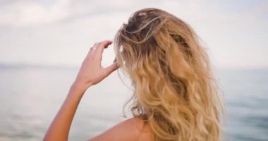 Bir kadın gün batımında sakin okyanusa bakarak suyun kenarında duruyor. Uzun saçları rüzgarda hafifçe savruluyor. Huzurlu manzarayı seyrederken, düşüncelere dalmış..