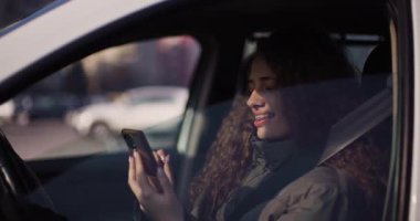 Diş teli takan neşeli genç bir kadın arabasının arka koltuğunda akıllı telefonunun keyfini çıkarıyor. Mutluluk ve bağlantı yayıyor..