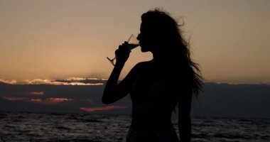 Bir insan canlı bir günbatımına karşı deniz kenarında duruyor. Güneş ufukta batarken huzurlu anın tadını çıkararak rahatlatıcı bir atmosfer yaratıyorlar..