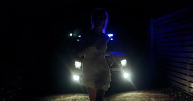 Genç bir kız yanıp sönen mavi ışıklarla polis arabasından fırlıyor. O kaçarken gece ayarı gergin bir atmosfer yaratıyor. Gölgeler onun kararlı yüz ve siluetinde oynar.