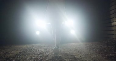 Karanlık ile çevrili çakıllı bir yolda huzurlu bir gece yürüyüşü. Farlar yankılandıkça ayak sesleri yankılanır. Yansıma için mükemmel gizemli bir atmosfer yaratır..