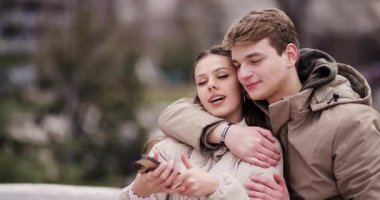 Genç bir adam ve bir kadın kentteki akıllı bir telefona bakıp samimi bir neşe ve bağlantı anını yakalarken birlikte gülüyorlar..