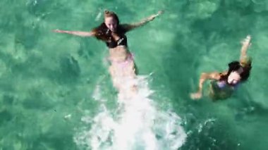 Yaz tatilinin tadını çıkaran iki genç kadın, yüzme ve turkuaz suda su sıçratma. Hava görünümü.