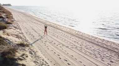 Bikinili genç bir kadın gün doğumunda boş bir kumsal boyunca yürür. Altın saat boyunca kaygısız bir sahil yürüyüşünün havadan görüntüsü..