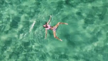Genç bir kadın güzel, berrak turkuaz suda yüzüyor ve eğleniyor. Doğrudan yukarıdan hava aracı görüntüsü. Huzurlu ve kaygısız.