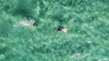 İki kadın zarifçe yüzüyor ve kristal gibi berrak bir tropik cennetin turkuaz sularında yüzüyorlar. Hava görünümü.