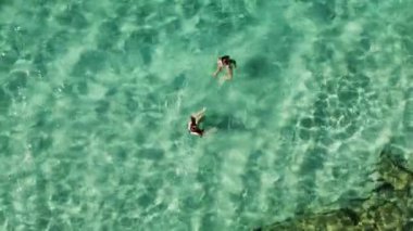 İki kadın okyanusun berrak turkuaz suyunun tadını çıkarıyor. Yaz tatilinde yüzen ve rahatlatan arkadaşların hava manzarası.