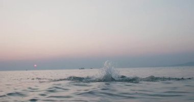 Denizde saldırganca su sıçratan bir adamın dinamik görüntüsü yumuşak bir günbatımı arka planına karşı özgürlük ve enerjiyi yansıtıyor..