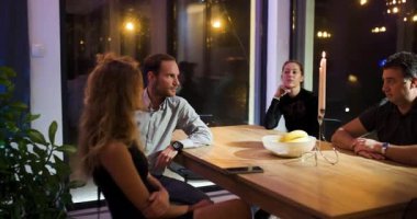 Arkadaşlar ve iş ortakları, mum ışığında ciddi ifadelerle fikirleri tartışmak üzere modern bir ev ofisinde gece yarısı bir toplantı için bir araya geldiler..