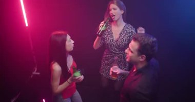 Arkadaşlar geceyi birlikte geçiriyorlar, renkli neon lambaların altında ellerinde içkilerle canlı bir kulüpte dans ediyorlar..