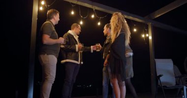 Arkadaşlar geceleri terasta içki içip sohbet etmekten zevk alıyorlar. Sıcak sicim ışıkları rahat bir atmosfer yaratır..