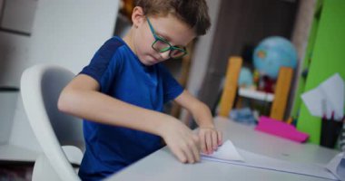 Gözlüklü genç bir çocuk odasında masasında oturmuş özenle origami yapıyor..