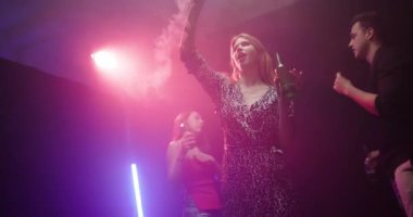 Dans eden ve gece kulübünde içmekten hoşlanan arkadaşlar. Genç bir kadın, renkli ışıklar ve müzikle kutlama yaparken havaya duman püskürtür..