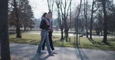 Genç bir çift güneşli bir günde parkta yürüyor, birbirlerine eşlik etmekten ve güzel manzaradan keyif alıyorlar..