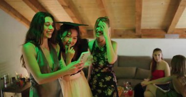 Üç genç kadın arkadaşlarının mezuniyetini kutluyor. Mezuniyet şapkası takıyor ve telefondaki fotoğraflara bakıyorlar..