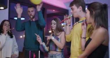 Bir ev partisinde doğum gününü kutlayan arkadaşlar. Parti üfleyicileri kullanıyorlar, alkışlıyorlar ve eğleniyorlar..