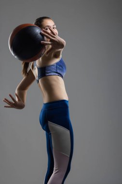 Spor sutyen ve tayt giymiş basketbol topu yakalayan genç bir kadının dinamik stüdyo çekimi. Güç ve çevikliğe odaklan..