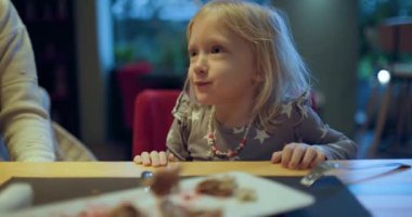 Küçük mutlu bir kız annesiyle bir restoranda yemek yiyor. Kahkahaları ve sohbetleri paylaşıyorlar, samimi bir an yaratıyorlar..