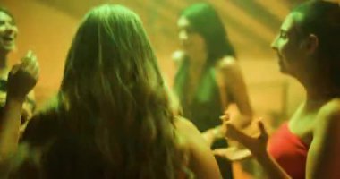 Genç bayan arkadaşlar birlikte dans ediyor ve bir partide eğleniyorlar. Renkli ışıklar sahneyi aydınlatıyor, canlı ve enerjik bir atmosfer yaratıyor..