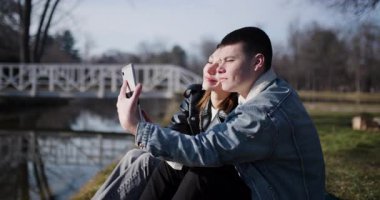 Genç bir çift selfie çeker ve nehir kenarında bir parkta hassas bir anı paylaşır..