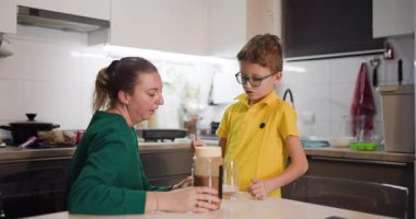 Bir anne ve oğlu mutfaklarında birlikte yemek hazırlıyorlar. Oğlu kavanoza şeker ekleyerek annesine yardım ediyor..