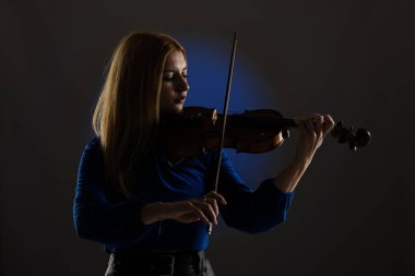 Beautiful blond girl playing violin. Female violinist against dark blue background.